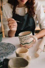 Potter draws an abstract design into earthenware cup. Experienced artist painting designs on...