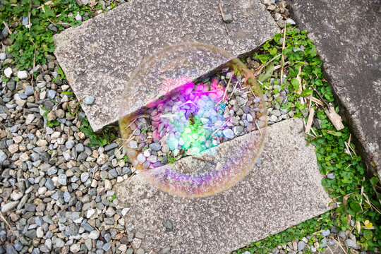 Iridescent Bubble on Pebbles and Concrete in an Outdoor Setting