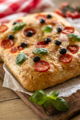 Focaccia - Italian Bread with tomatoes basil leaves olives and olive oil on cutting board