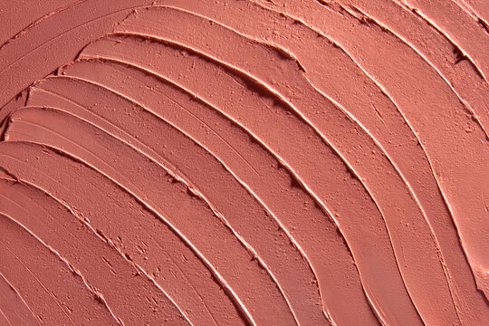 Textured background of pale red lipstick, smeared randomly in curves