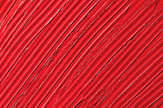 Wavy textured background of red lipstick smeared on flat surface. 