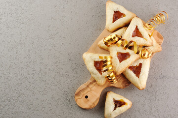 Close up freshly baked triangular cookies filled with fruit surrounded by golden decorations ribbon on a wooden cutting board Purim celebration concept. top view