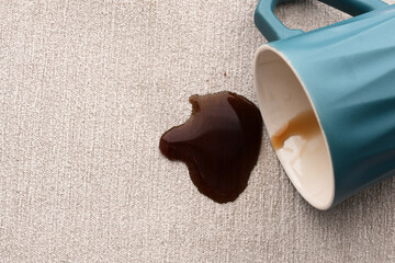 A turquoise mug overturned, spilling coffee onto a textured gray surface. The mess reflects a...