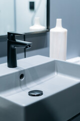 modern bathroom sink with sleek black faucet, white ceramic bottle, and mirror in background, creating minimalist and elegant design