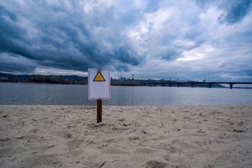 A cautionary sign stands prominently in the sandy foreground as stormy clouds ominously loom over a...