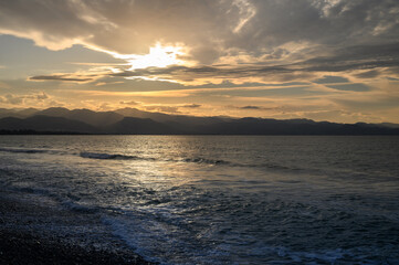 Golden sunset over tranquil waves and distant mountains along a serene coastline