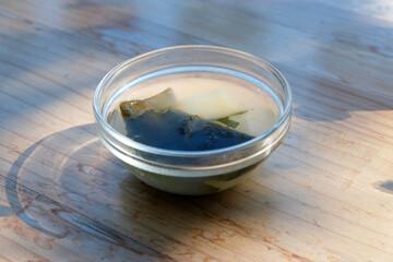 Wakame seaweed soup in a clear cup on a wooden table close up selective focus with its reflective , day light 