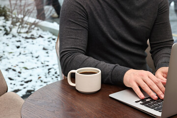 Businessman typing on laptop during coffee break at wooden table in cafe, closeup