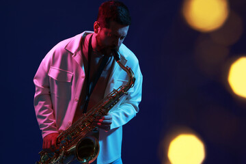 Obraz premium Professional musician playing saxophone on blue background with blurred lights. Bokeh effect