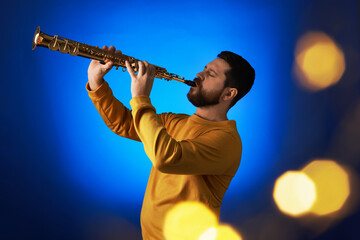 Professional musician playing soprano saxophone on blue background with blurred lights. Bokeh effect