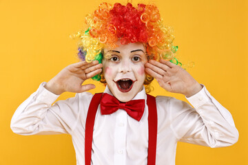 Emotional little boy dressed like clown on yellow background. Surprise party