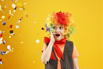 Surprised boy dressed like clown and flying confetti on orange background. Surprise party