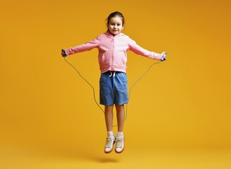Cute little girl with jump rope on yellow background