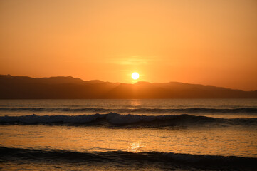 Golden sunset paints the horizon with warm hues over calm ocean waves