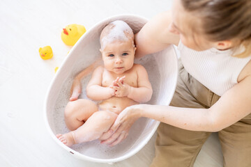 mom's hands bathe a small newborn baby in a bubble bath, washing the baby