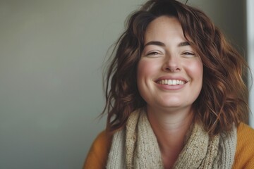 Naklejka premium A smiling young Caucasian woman with curly brown hair, wearing a cozy sweater and scarf, radiates warmth and joy.