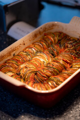 A close-up of a baked ratatouille dish with sliced zucchini, tomatoes, and eggplant arranged in a...