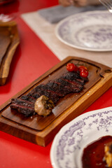 A grilled steak with a charred crust, paired with roasted garlic and cherry tomatoes, served on a wooden board in a fine dining setting.