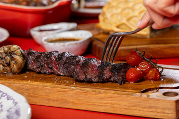 A grilled steak with a charred crust, paired with roasted garlic and cherry tomatoes, served on a wooden board in a fine dining setting.