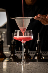 A bartender straining a cocktail into a glass using a fine mesh strainer, showcasing professional...
