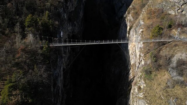 Saillon, Switzerland - 15 February 2025: Tourists Walking Across the Passerelle &agrave; Farinet, a Wooden Bridge Above the Salentse Gorge with Views of the Swiss Alps on a Beautiful Sunny Day
