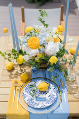 Name card lies next to an olive branch and a lemon on a plate on a set table near a colorful bouquet of flowers
