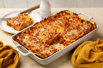 Lunch with homemade Red Lentil Lasagne. Vegetarian dish made with vegetables, lentils and tomato ragu and is topped with a creamy cheese topping. Beige table.