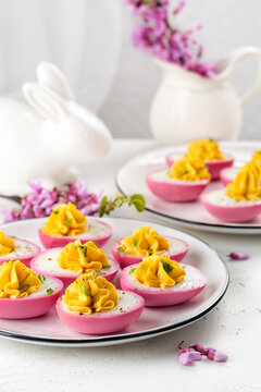 Easter dinner. Stuffed Pink Boiled Deviled  Eggs with pepper and mayonnaise colored with beetroot. Easter bunny and spring flowers. Vertical iage.