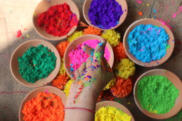 Colorful hands covered in gulal forming a heart shape with fingers, vibrant Holi background, festive mood, love and celebration. Selective focus 