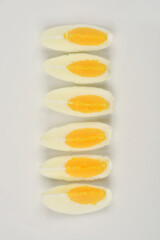 A top-down shot of slices of hard-boiled egg arranged in a row on a white plate, showing their creamy white and bright yellow yolks