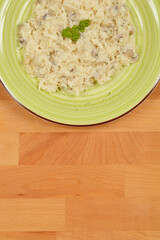 A top-down shot of a light-colored mushroom risotto served on a green plate, placed on a wooden surface