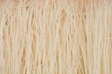 A flat lay close-up of a bundle of thin, raw rice noodles, revealing their fine texture and light, off-white hue