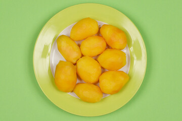A top-down shot of several cooked yellow potatoes arranged on a white plate with a green rim, placed against a green background