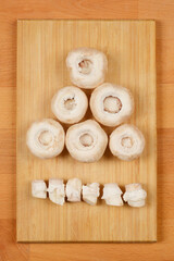 A top-down view of six white button mushrooms with their stems removed, arranged in a triangular shape above a row of mushroom stems, on a wooden cutting board