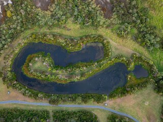 Aerial view of a wetland area in New Zealand. The image shows a winding pond surrounded by lush vegetation and walking paths, promoting conservation and recreation. Te Atatu Peninsula, Auckland, NZ