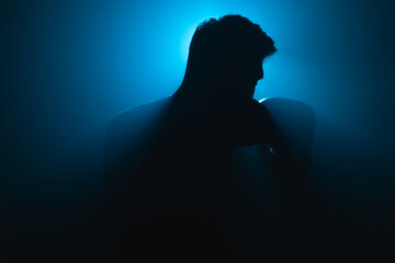 Silhouette of an Asian male boxer in fighting stance, lit by dramatic blue backlight and surrounded...