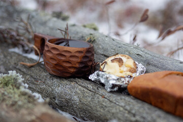 A wooden cup with tasty coffee stands on a log in the winter forest.