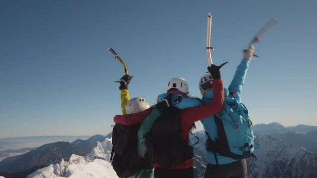 Three people celebrate reaching the summit of a snowy mountain, holding ski poles and wearing backpacks.