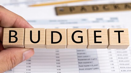 financial planning expenses protection concept. Hand holding wooden blocks spelling "BUDGET" over a financial document.