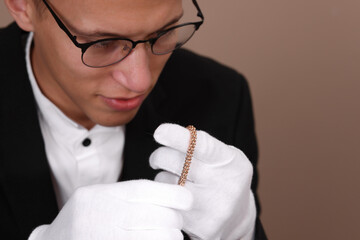 Appraiser evaluating luxury jewelry on beige background, closeup