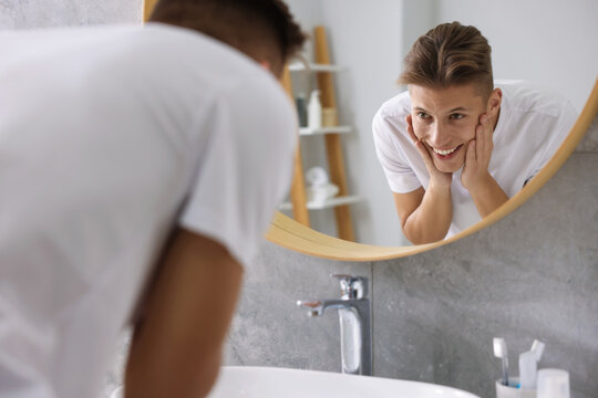 Washing face. Happy man looking at mirror in bathroom