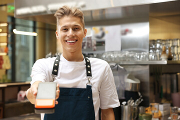 Smiling cafe worker with payment terminal indoors