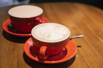 Two red cups of coffee on wooden table showcasing intricate latte art.