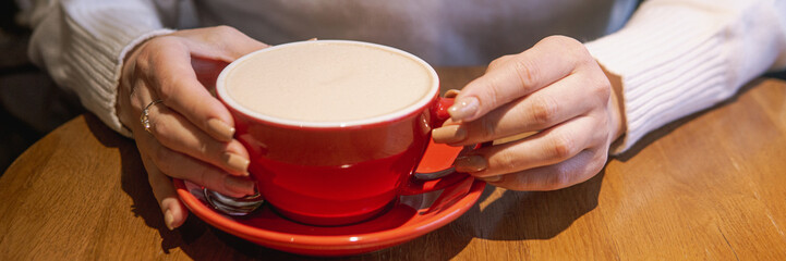 A cozy scene showing hands holding a red cup of a beverage on a wooden surface, highlighting a warm and inviting ambiance.