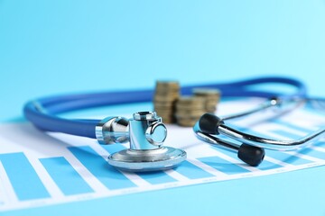 Stethoscope, chart and coins on light blue background, closeup
