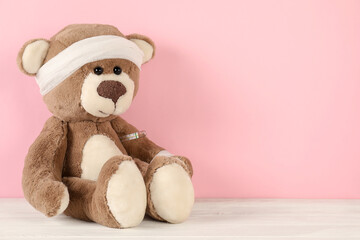 Fototapeta premium Teddy bear with bandages and thermometer on white wooden table against pink background, space for text