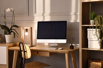 Comfortable workplace with modern computer and lamp on wooden desk in home office