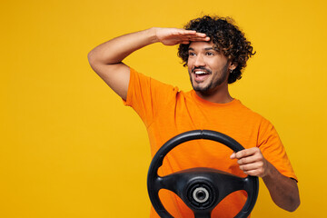 Young smiling happy fun Indian man he wear orange t-shirt casual clothes hold steering wheel...