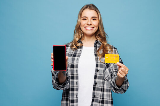 Young woman wears grey shirt casual clothes using blank scren mobile cell phone hold credit bank card shopping online order delivery booking tour isolated on plain blue background. Lifestyle concept.