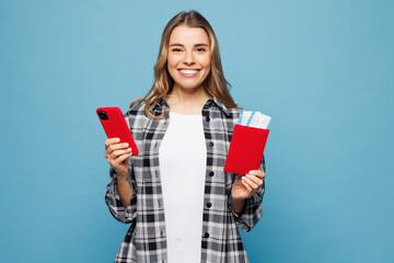 Traveler woman wear grey casual clothes hold passport ticket use mobile cell phone isolated on plain blue background. Tourist travel abroad in free time rest getaway. Air flight trip journey concept.